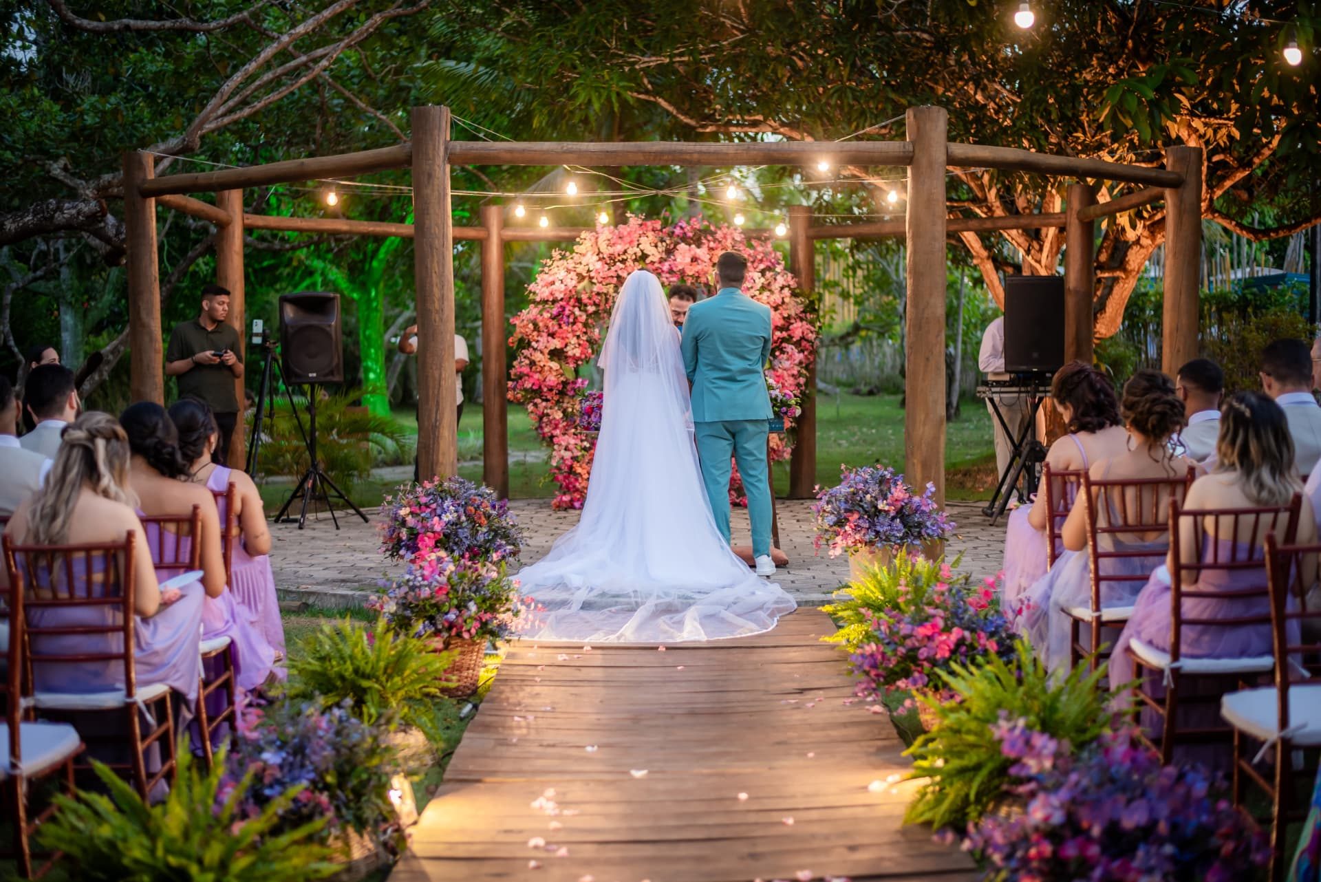 Noivos no altar de madeira com arco de flores rosas e caminho iluminado na Chácara Campos Elísios